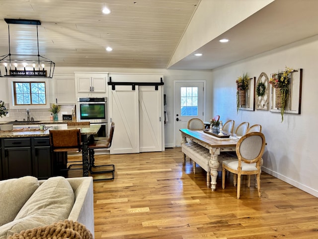 dining space with recessed lighting, a barn door, an inviting chandelier, light wood finished floors, and baseboards