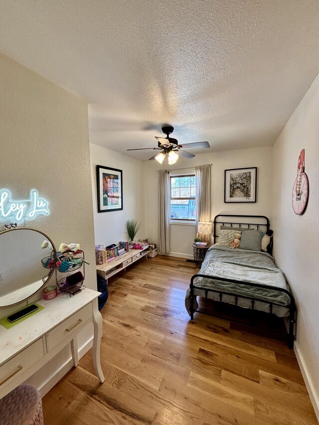 bedroom featuring baseboards, a textured ceiling, light wood-style flooring, and a ceiling fan