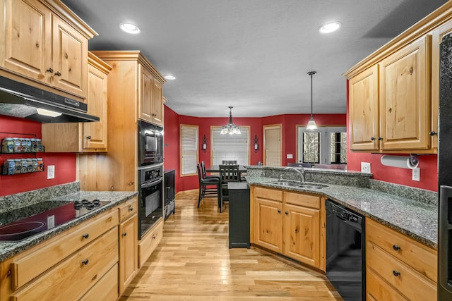 kitchen with dark stone counters, sink, black appliances, pendant lighting, and light hardwood / wood-style flooring