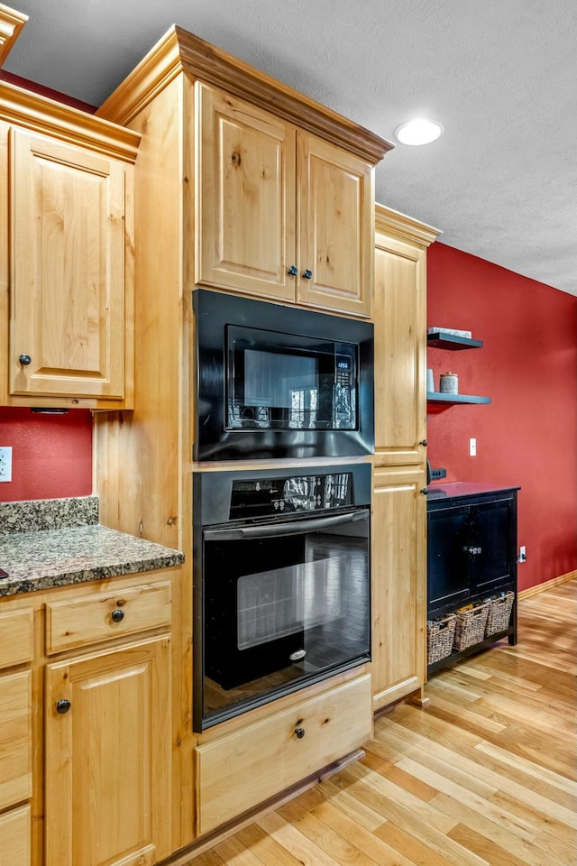 kitchen with black appliances, light stone counters, light wood-type flooring, and a textured ceiling