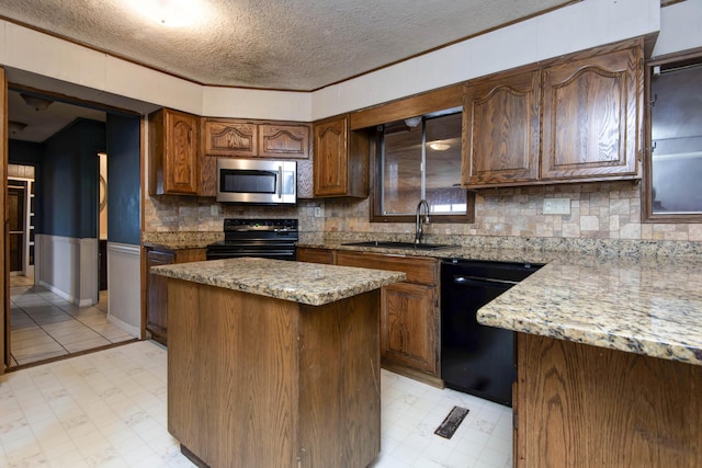 kitchen featuring light stone counters, a textured ceiling, sink, black appliances, and a center island