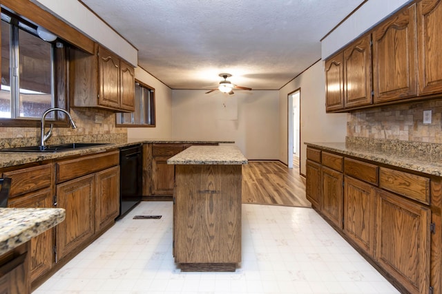 kitchen with ceiling fan, sink, a center island, light stone countertops, and black dishwasher