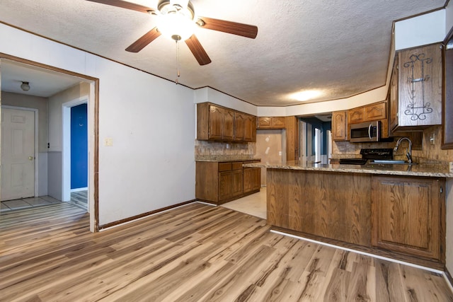 kitchen featuring sink, black range oven, light hardwood / wood-style flooring, backsplash, and kitchen peninsula