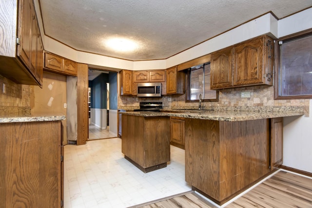 kitchen with a textured ceiling, light hardwood / wood-style flooring, a kitchen island, and sink