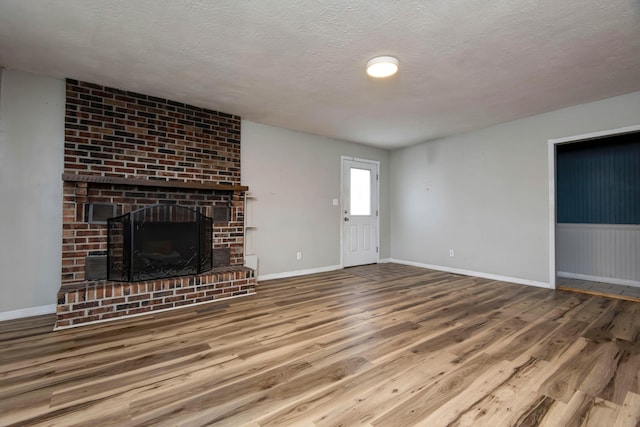 unfurnished living room with a brick fireplace, a textured ceiling, and hardwood / wood-style flooring