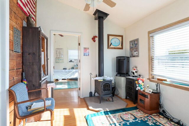 interior space featuring light wood-type flooring, a wood stove, ceiling fan, and lofted ceiling