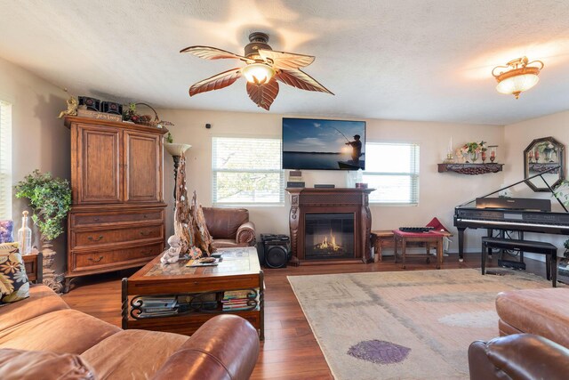 living room with a textured ceiling, ceiling fan, and dark wood-type flooring