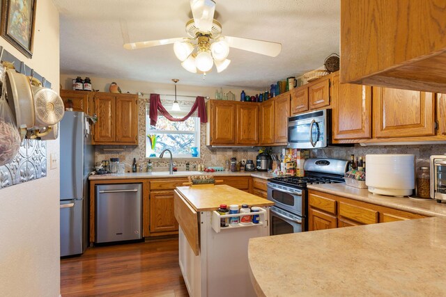 kitchen with decorative backsplash, appliances with stainless steel finishes, ceiling fan, dark wood-type flooring, and sink