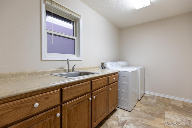 clothes washing area with a textured ceiling, cabinets, independent washer and dryer, and sink