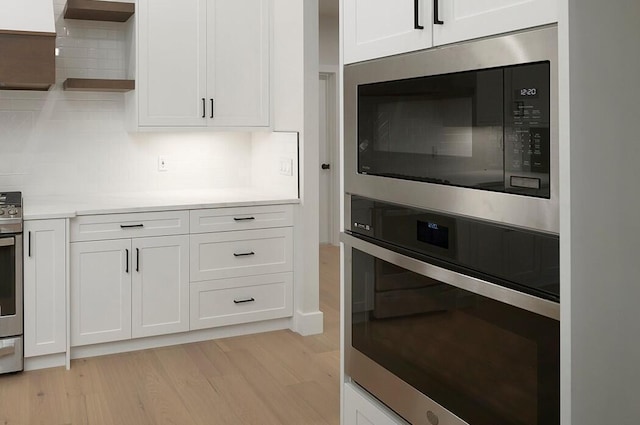 kitchen with decorative backsplash, white cabinets, stainless steel appliances, and light hardwood / wood-style floors