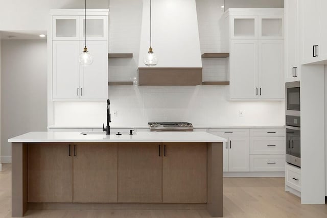 kitchen with light hardwood / wood-style floors, white cabinetry, sink, and an island with sink