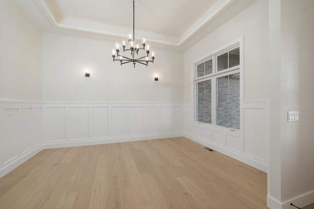 unfurnished dining area with a chandelier, light hardwood / wood-style floors, and a tray ceiling