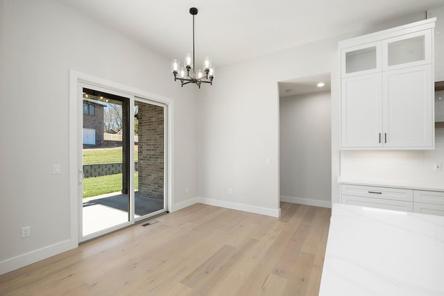 unfurnished dining area with light wood-type flooring and a notable chandelier