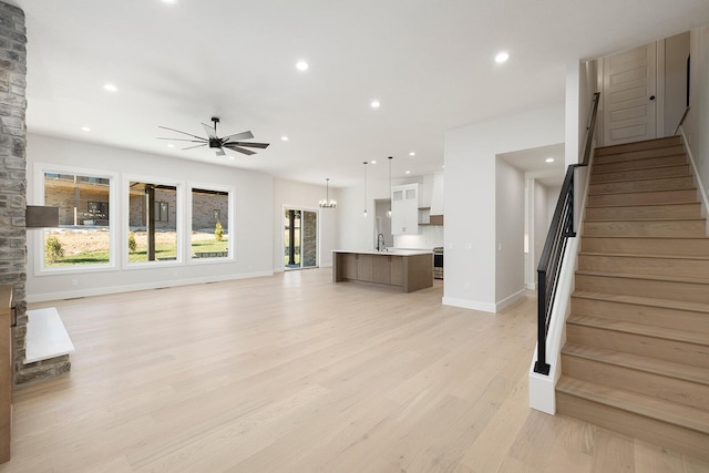 unfurnished living room with ceiling fan with notable chandelier, light wood-type flooring, and sink