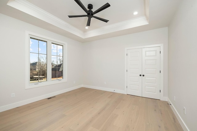 unfurnished bedroom featuring ceiling fan, crown molding, light hardwood / wood-style flooring, and a tray ceiling