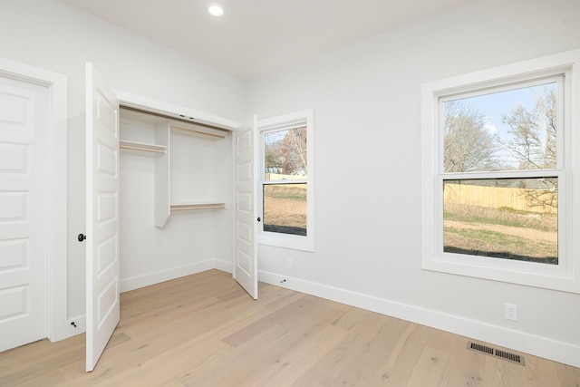 unfurnished bedroom with a closet, light hardwood / wood-style flooring, and multiple windows