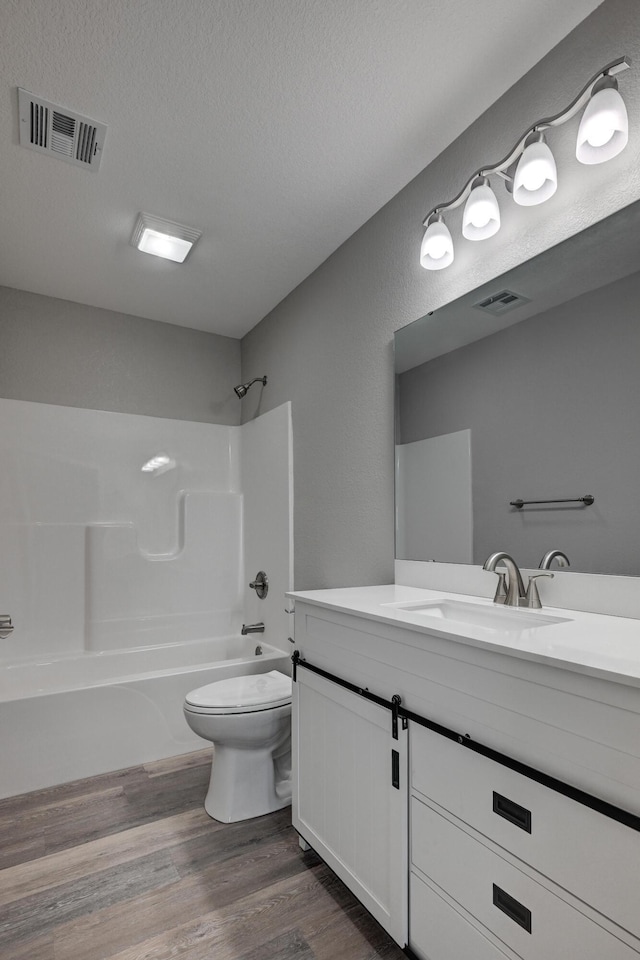 full bathroom featuring toilet, vanity, hardwood / wood-style floors, tub / shower combination, and a textured ceiling