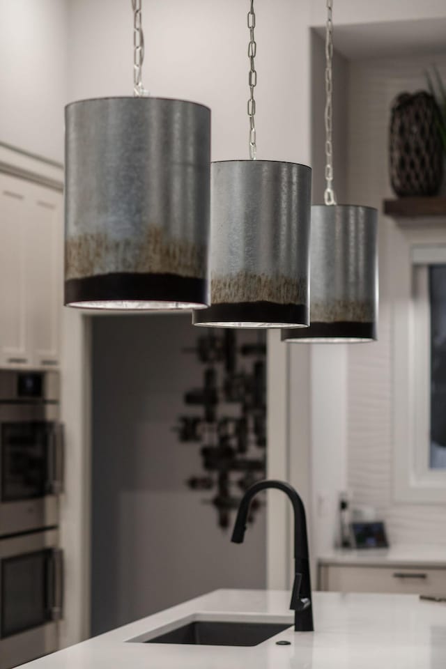 kitchen featuring pendant lighting, white cabinetry, sink, and double oven