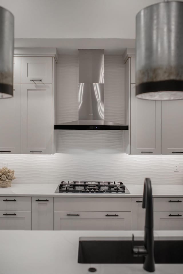 kitchen featuring black gas stovetop, sink, white cabinets, and wall chimney range hood