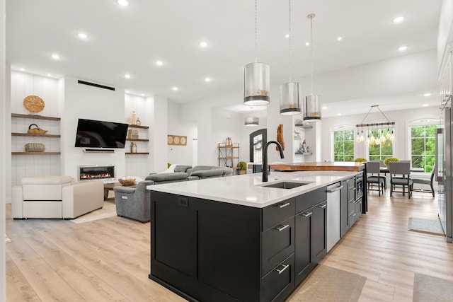 kitchen with a kitchen island with sink, sink, pendant lighting, and light hardwood / wood-style floors