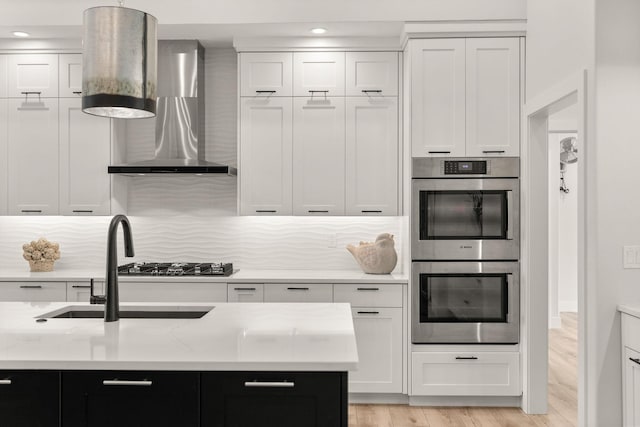 kitchen featuring white cabinets, stainless steel double oven, light hardwood / wood-style floors, and wall chimney exhaust hood