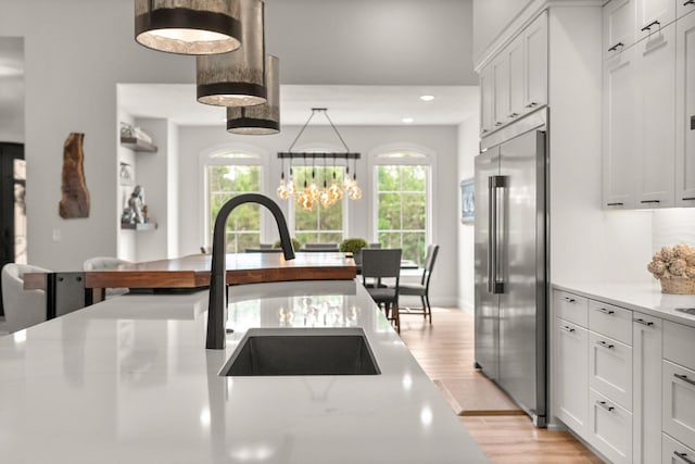 kitchen with light wood-type flooring, light stone counters, an inviting chandelier, white cabinets, and built in fridge