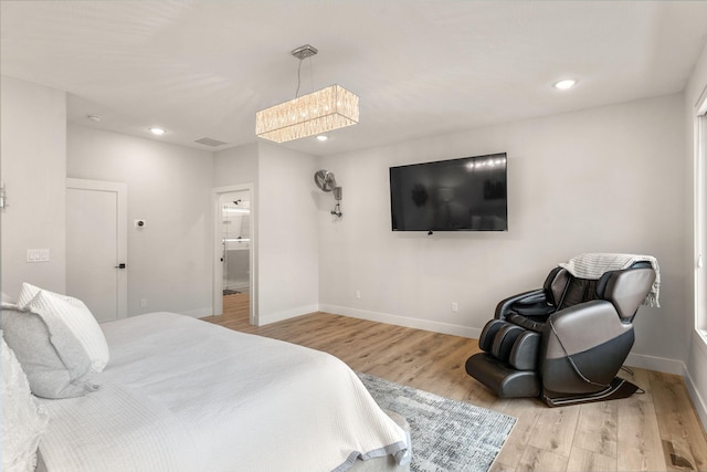 bedroom with ensuite bathroom, a notable chandelier, and light wood-type flooring