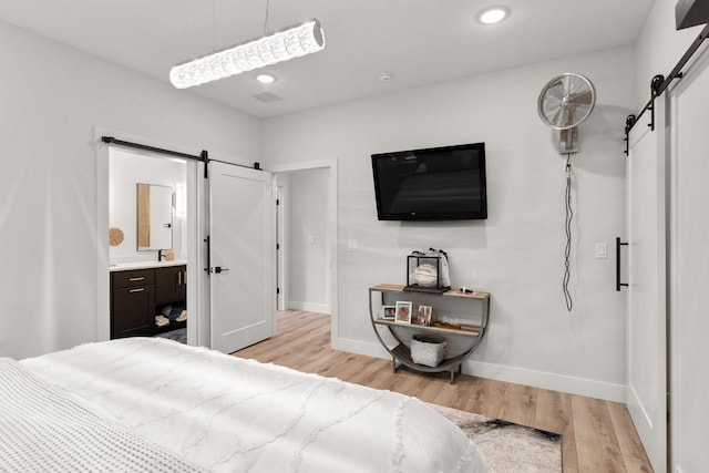 bedroom featuring ensuite bathroom, a barn door, light wood-type flooring, and sink