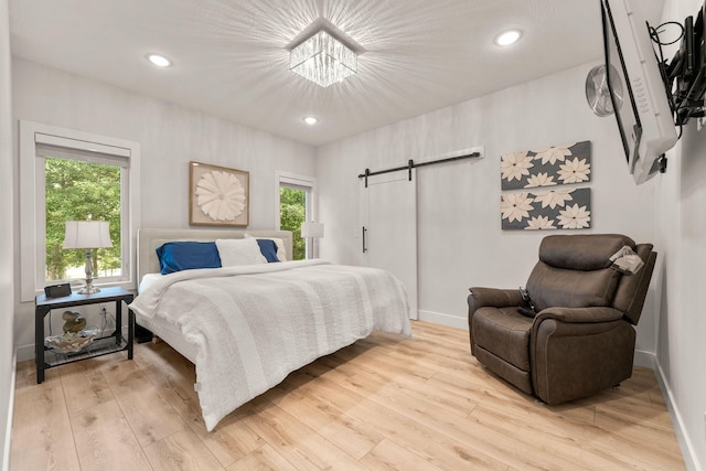 bedroom featuring light hardwood / wood-style floors, a barn door, and multiple windows