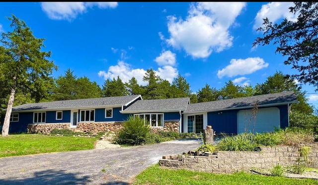 ranch-style home featuring an attached garage, stone siding, driveway, and a front lawn