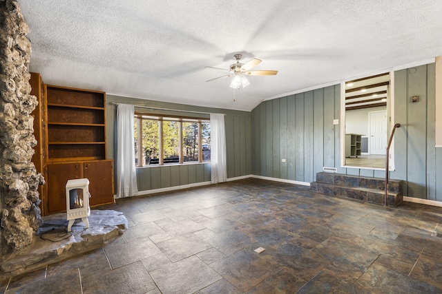 unfurnished living room featuring ceiling fan, lofted ceiling, wooden walls, heating unit, and a wood stove