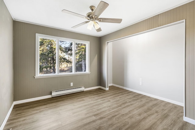 spare room with baseboard heating, wood finished floors, a ceiling fan, and baseboards