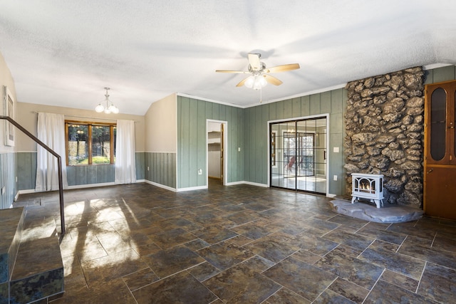 unfurnished living room featuring a wood stove, a wainscoted wall, a textured ceiling, and ceiling fan with notable chandelier