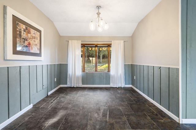 spare room with vaulted ceiling, stone finish floor, wainscoting, and a notable chandelier