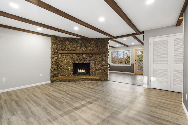 unfurnished living room featuring light hardwood / wood-style flooring, beam ceiling, and a stone fireplace