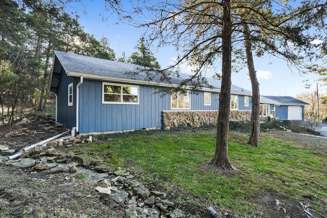 view of front of home with stone siding, a shingled roof, and a front yard