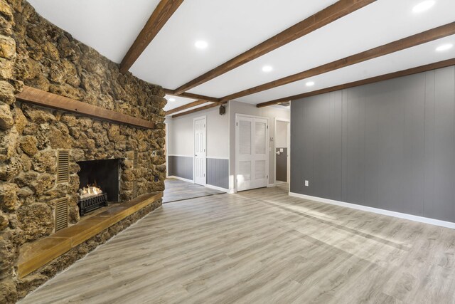 unfurnished living room featuring a stone fireplace, light wood-type flooring, and beam ceiling