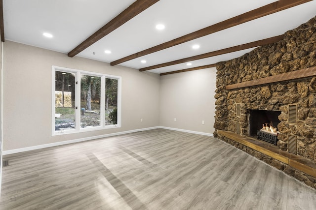 unfurnished living room with hardwood / wood-style floors, beamed ceiling, and a stone fireplace