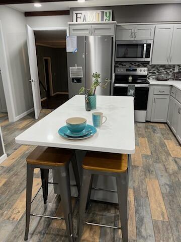 kitchen featuring stainless steel appliances, wood finished floors, gray cabinets, and tasteful backsplash