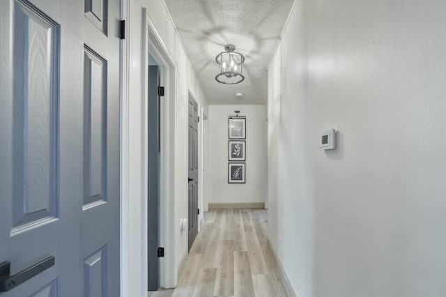 corridor featuring light wood-type flooring, a textured ceiling, and an inviting chandelier