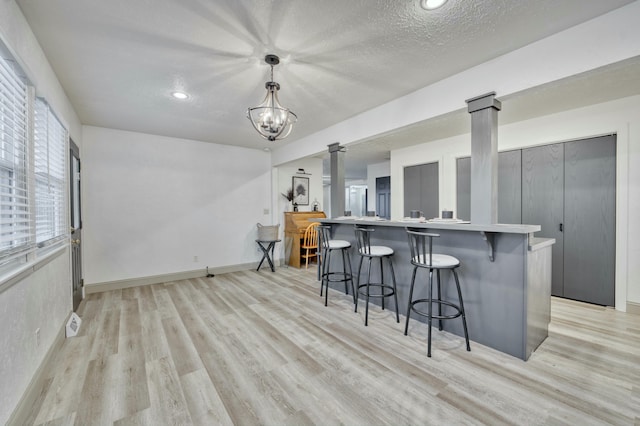 kitchen with a textured ceiling, decorative light fixtures, light hardwood / wood-style floors, a breakfast bar area, and a chandelier