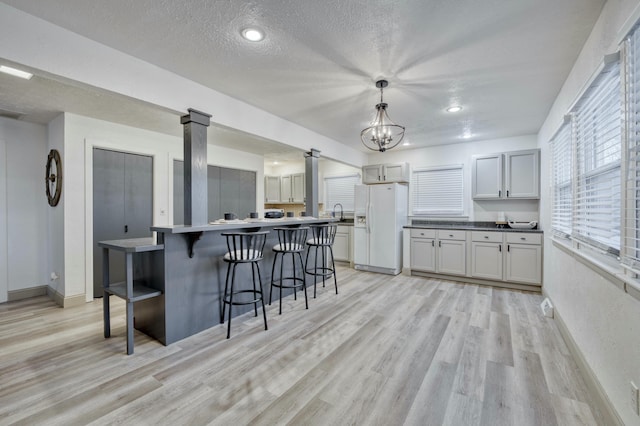 kitchen with a center island, hanging light fixtures, light wood-type flooring, a textured ceiling, and white fridge with ice dispenser