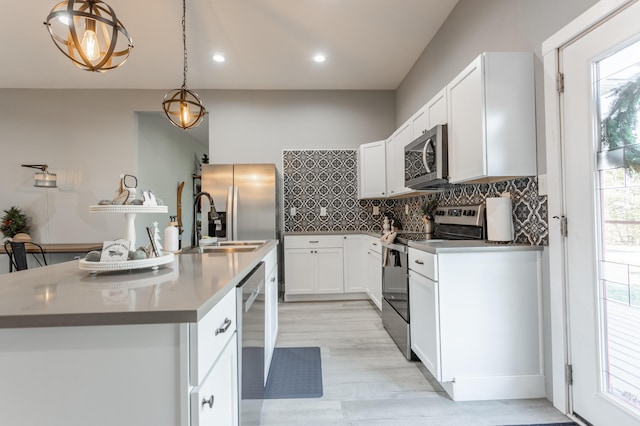 kitchen featuring pendant lighting, stainless steel appliances, white cabinetry, and a center island with sink