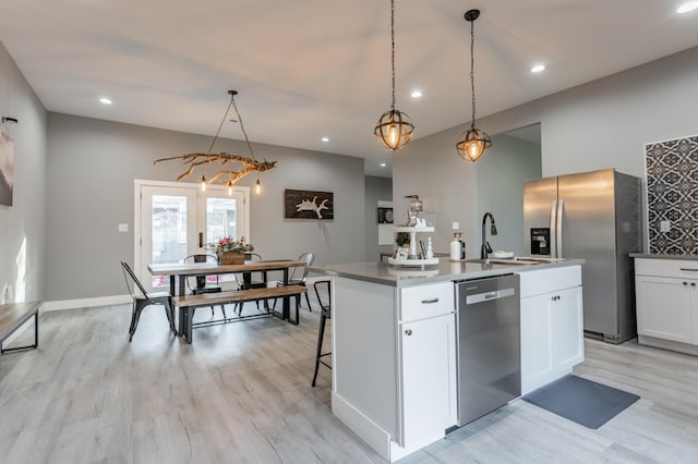 kitchen with a kitchen island with sink, white cabinets, sink, decorative light fixtures, and stainless steel appliances