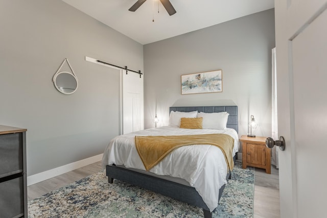 bedroom featuring a barn door, light hardwood / wood-style floors, and ceiling fan