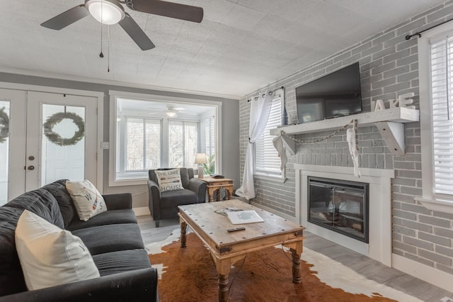 living room featuring a large fireplace, french doors, brick wall, crown molding, and light hardwood / wood-style floors