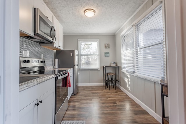 kitchen featuring white cabinets, stainless steel appliances, dark hardwood / wood-style floors, and crown molding