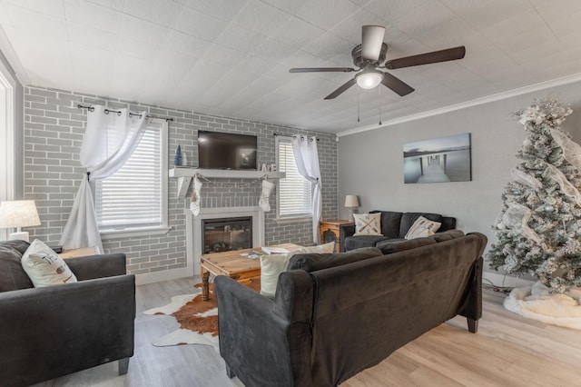 living room with brick wall, ceiling fan, crown molding, light hardwood / wood-style flooring, and a fireplace