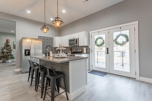 kitchen featuring white cabinetry, pendant lighting, a kitchen island with sink, appliances with stainless steel finishes, and light wood-type flooring