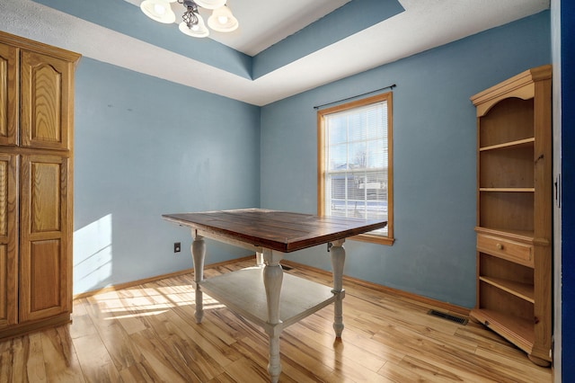 unfurnished office featuring a tray ceiling, a notable chandelier, and light wood-type flooring